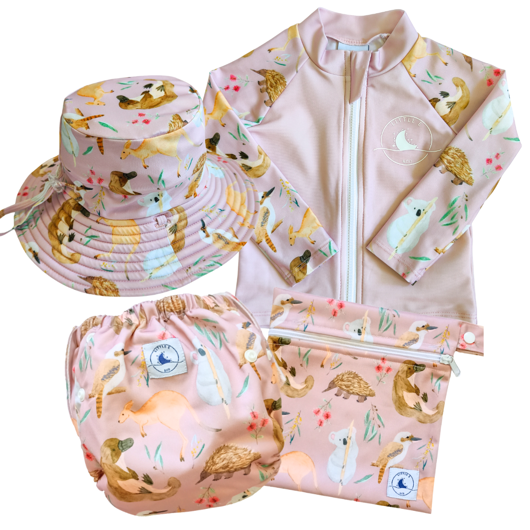 LITTLE E & CO - four-piece kids' swim set featuring a long-sleeve rash guard, swim hat, swim nappy and wet bag. The set is a pale pink with a colourful Australian animals print featuring koalas, kangaroos, platypus, kookaburras and echidnas. Made with UPF 50+ sun protection fabric. The rash guard has a front zipper for easy wear, and the swim nappy has adjustable snaps, and the hat has adjustable toggles.