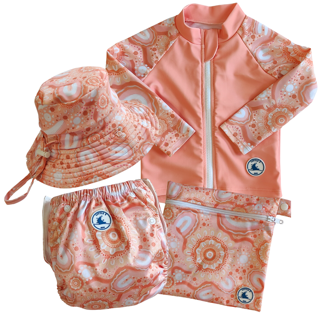 Baby Swimwear Set in peach pink with contemporary indigenous print, featuring UPF 50+ long sleeve rashie with front zipper, adjustable swim nappy, sun hat with toggles, and matching wet bag.
