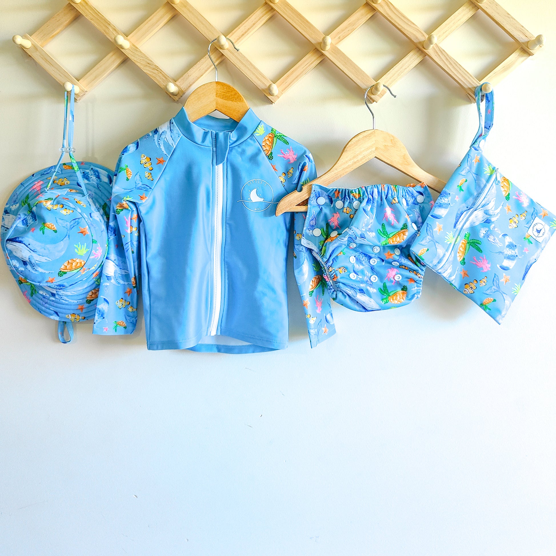Baby Swimwear Set in blue ocean print with whales, turtles, fish, and coral, includes UPF 50+ long sleeve rashie with front zipper, adjustable swim nappy, sun hat with toggles, and matching wet bag.
