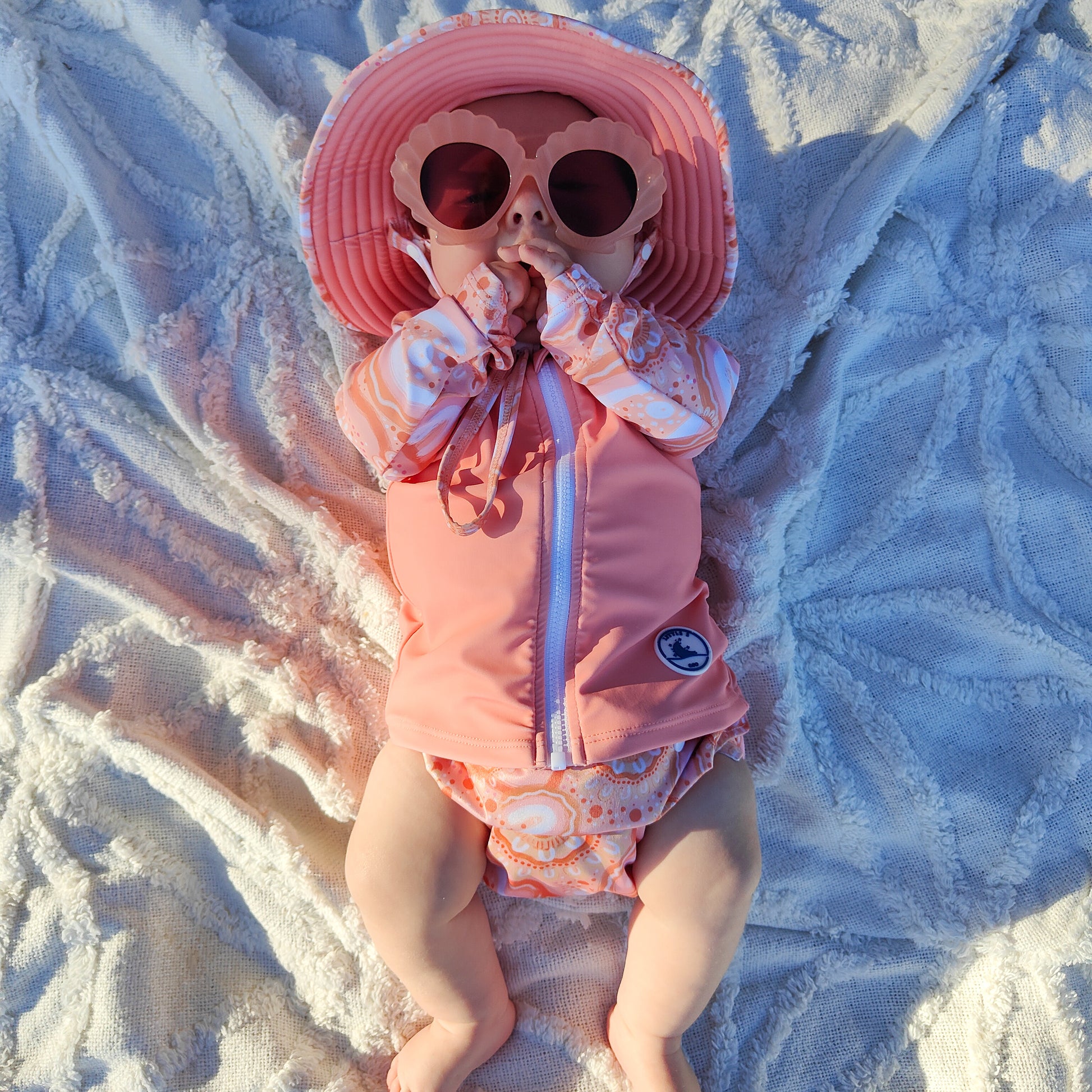 Baby Swimwear Set in peach pink with colourful Indigenous print, worn by baby, featuring long sleeve rashie and reusable swim nappy.