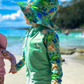 Baby Swimwear Set in green rainforest print with UPF 50+ rashie, reusable swim nappy, sun hat, and wet bag, worn at the beach.