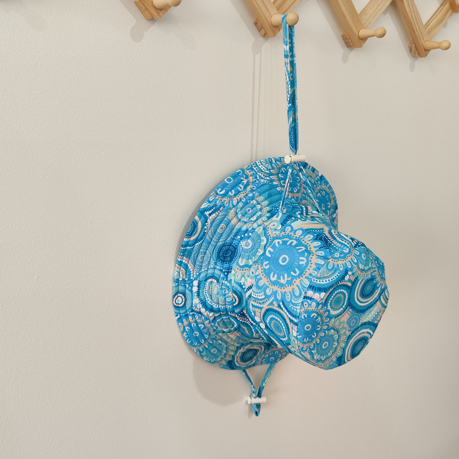 Kids swim hat in turquoise blue with colourful contemporary Indigenous print, featuring UPF 50+ fabric and adjustable toggles.