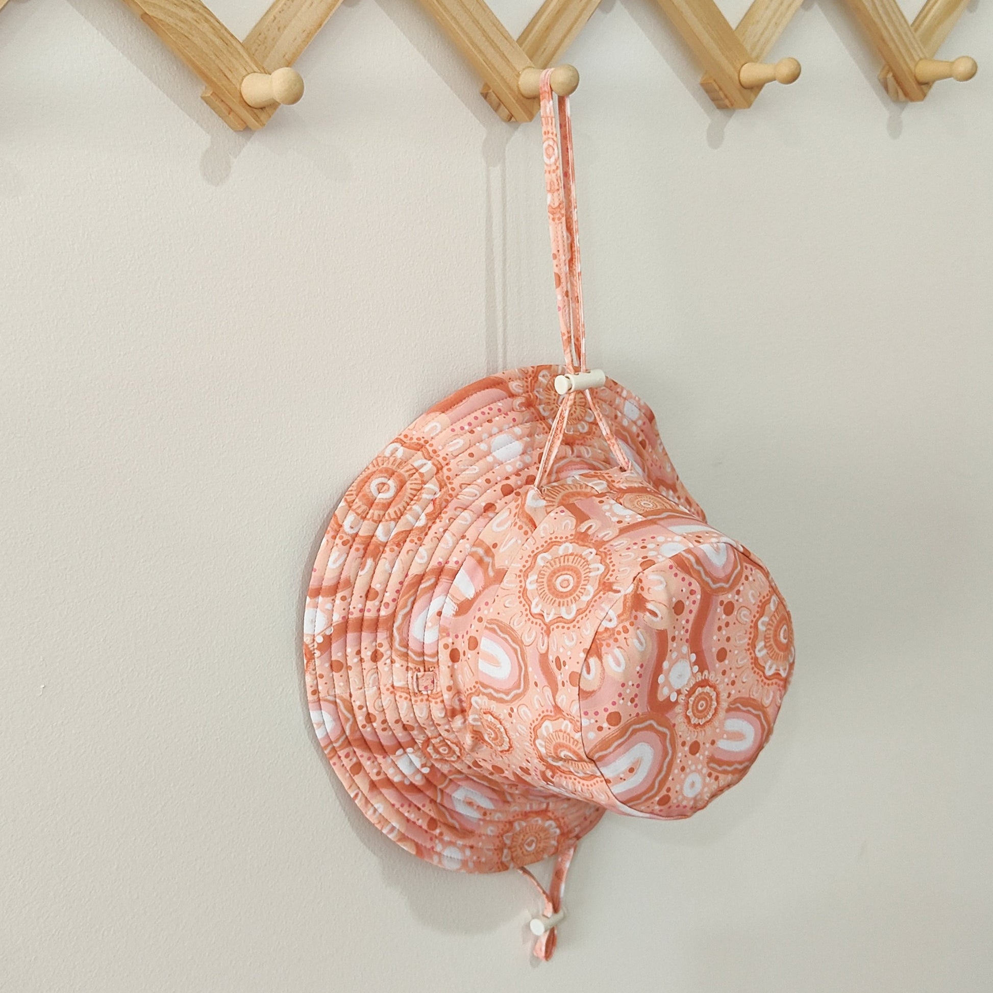 Kids swim hat in peach pink with contemporary indigenous print, featuring UPF 50+ fabric and adjustable toggles for a secure fit.