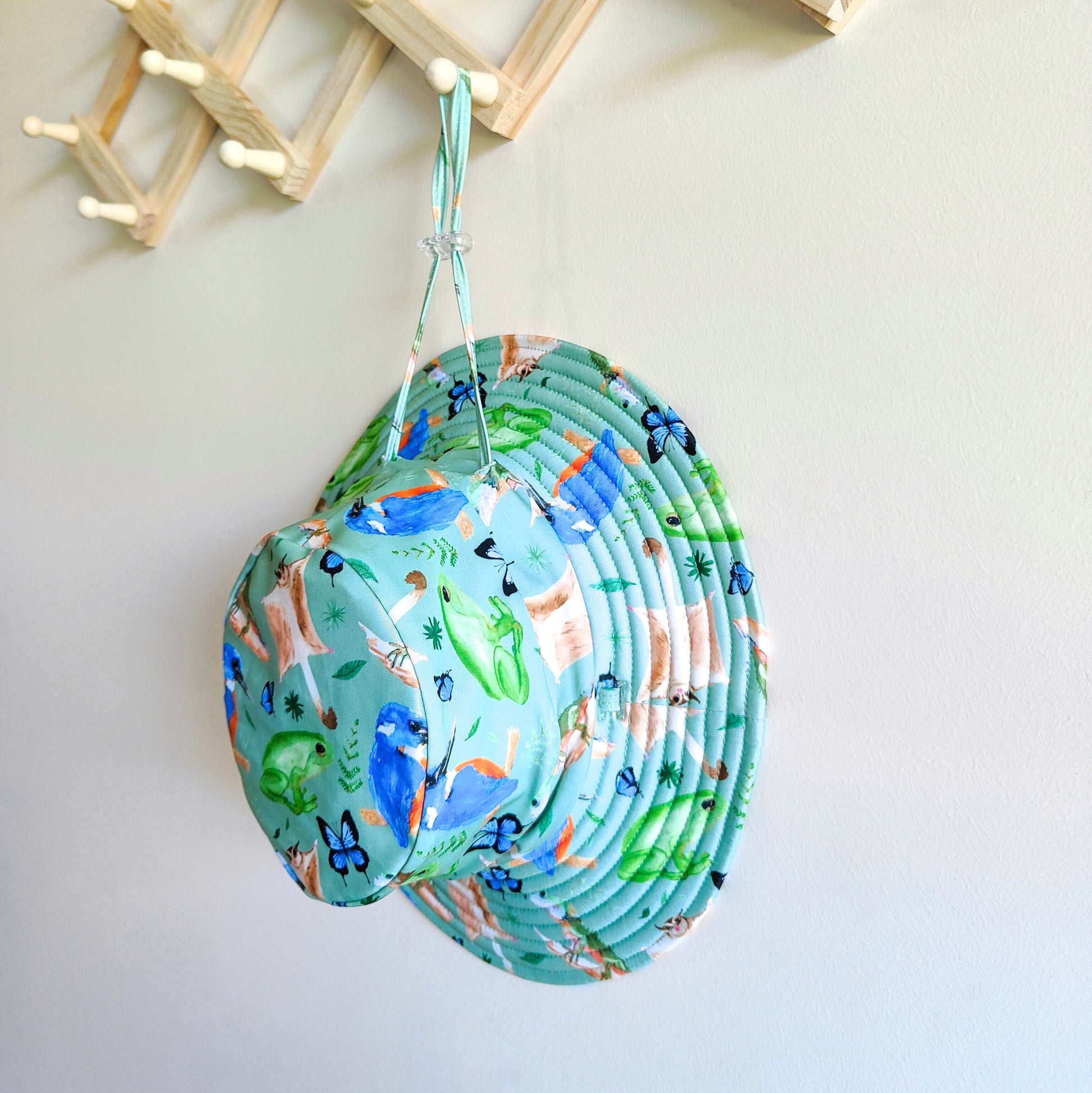 LITTLE E & CO – kids swim hat, a green with a colourful rainforest print featuring birds, frogs, lizards and butterflies. Made with UPF 50+ sun protection fabric. The swim hat features adjustable toggles.