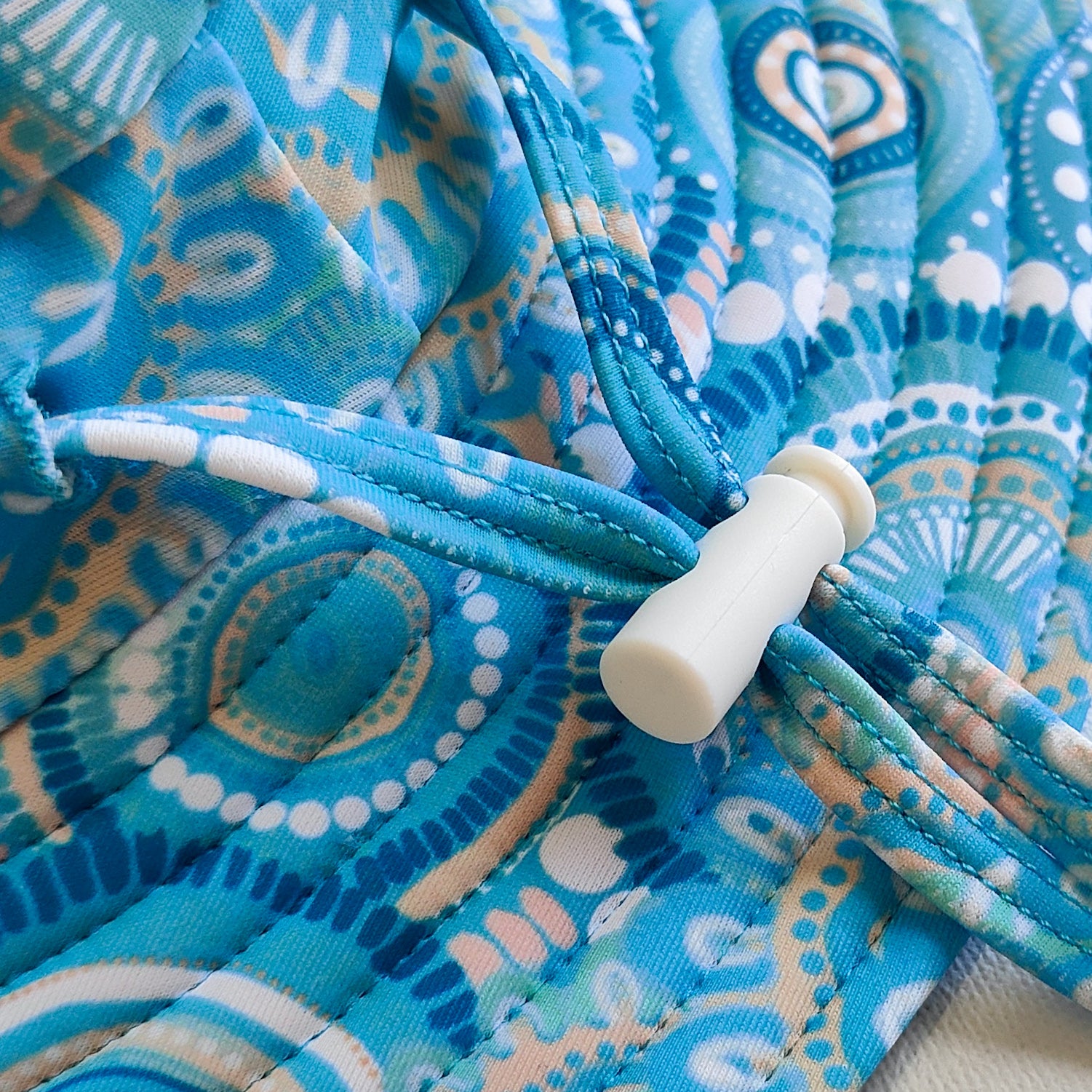 Kids swim hat in turquoise blue with colourful contemporary Indigenous print, featuring UPF 50+ fabric and adjustable toggles.