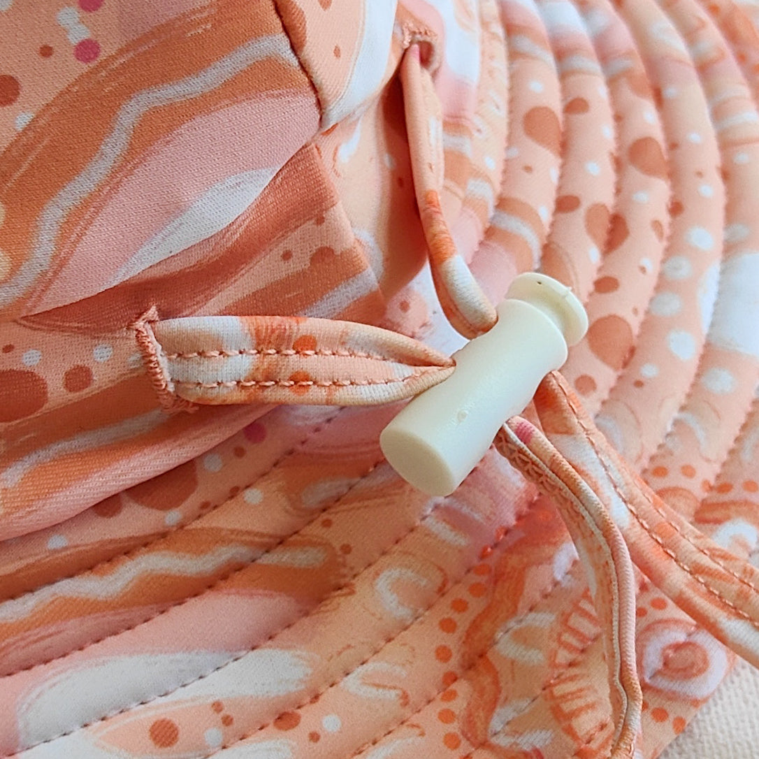 Kids swim hat, a peach pink with a colourful contemporary indigenous print. Made with UPF 50+ sun protection fabric. The swim hat features adjustable toggles.