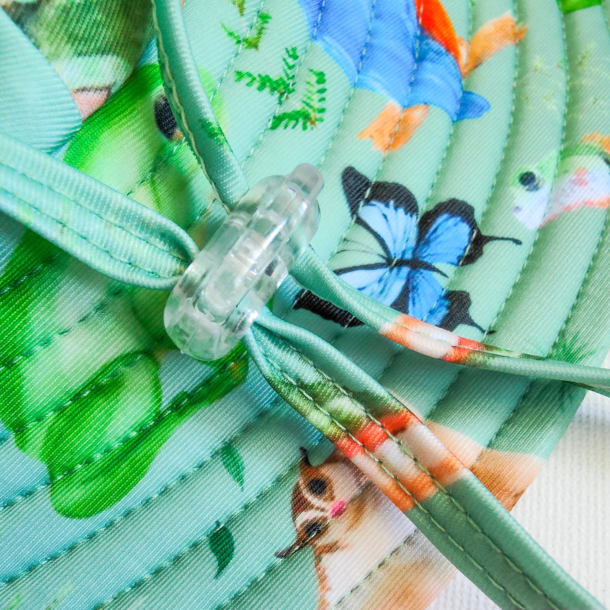 LITTLE E & CO – kids swim hat, a green with a colourful rainforest print featuring birds, frogs, lizards and butterflies. Made with UPF 50+ sun protection fabric. The swim hat features adjustable toggles.