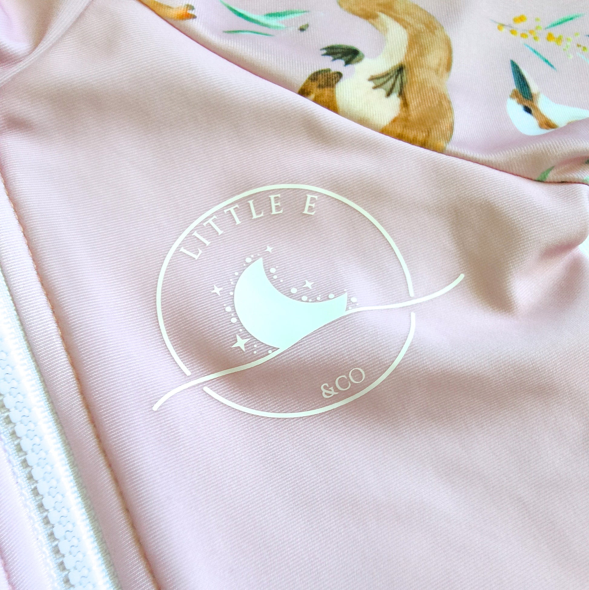 LITTLE E & CO – kids long-sleeve rash guard, a pale pink with a colourful Australian animals print featuring koalas, kangaroos, platypus, kookaburras and echidnas. Made with UPF 50+ sun protection fabric. The rash guard has a front zipper for easy wear.