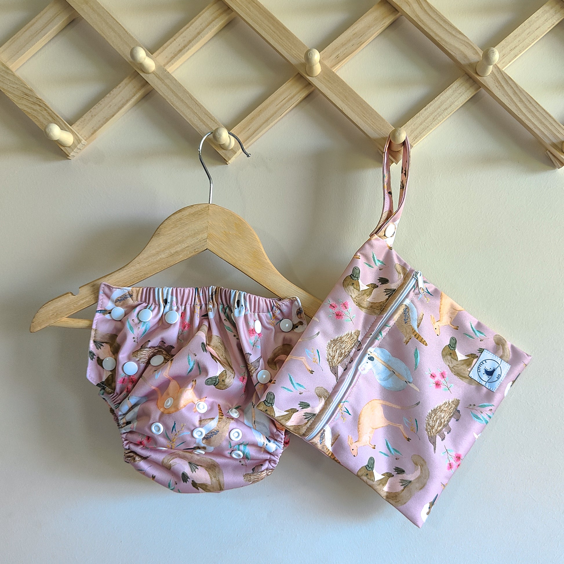 Swim nappy and wet bag in pale pink with colourful Australian animals print, including koalas, kangaroos, and echidnas. Features adjustable snaps for a secure fit.