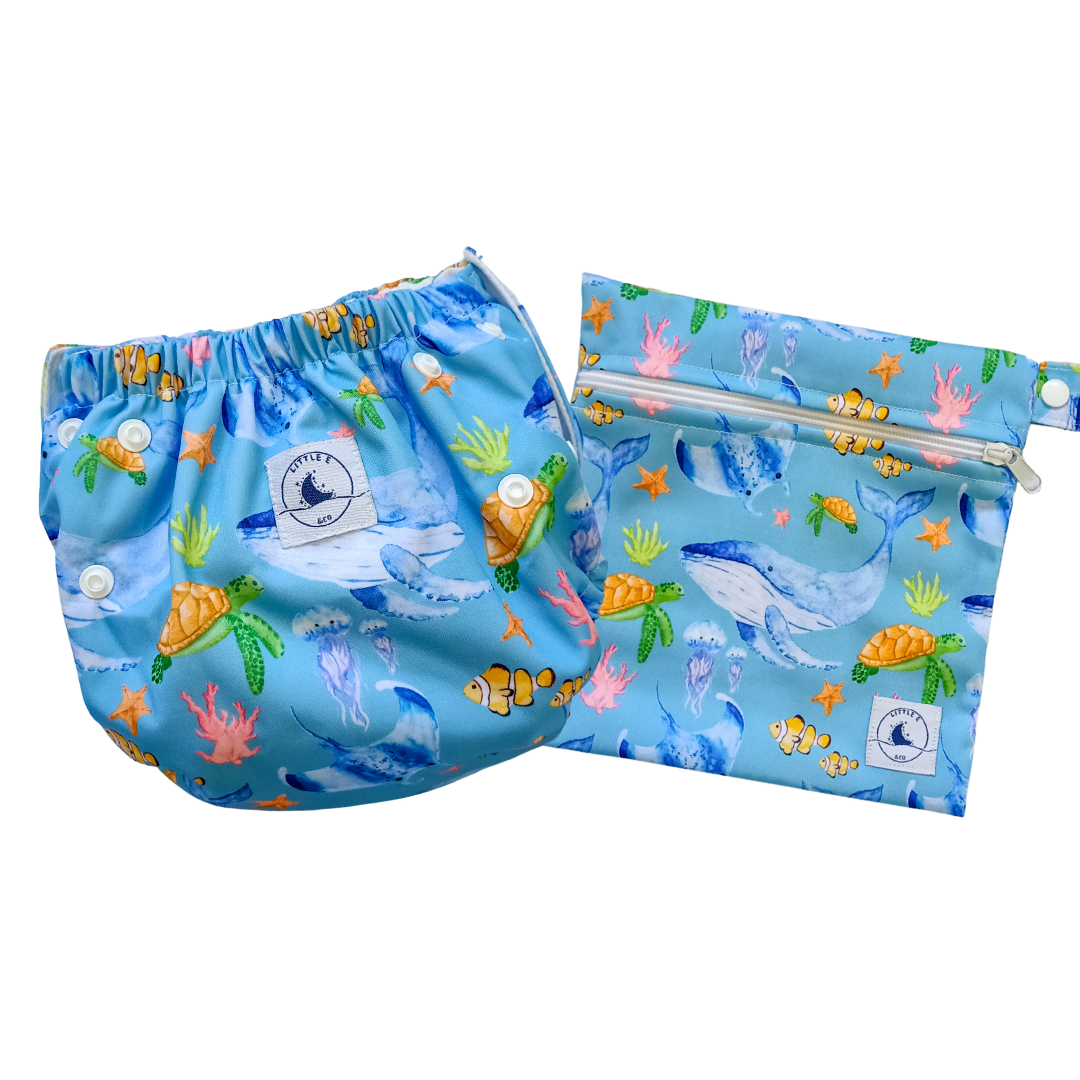 Swim Nappy and Wet Bag in blue ocean print with whales, turtles, fish, and coral, featuring one-size swim nappy with adjustable snaps and waterproof wet bag with strap.