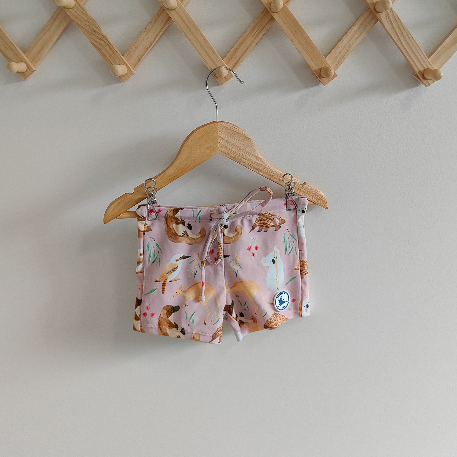 Kids swim shorts in pale pink with Australian animals print, featuring koalas, kangaroos, platypus, kookaburras, and echidnas, made with UPF 50+ fabric and adjustable drawstring waistband.