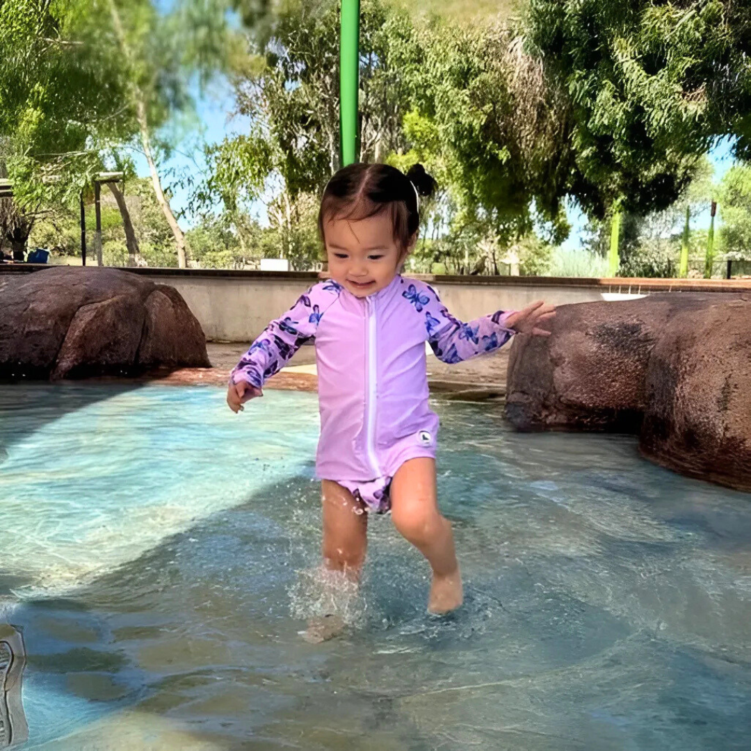 Baby swimwear set in butterflies print worn by toddler playing in shallow water, featuring long sleeve rashie and swim nappy.