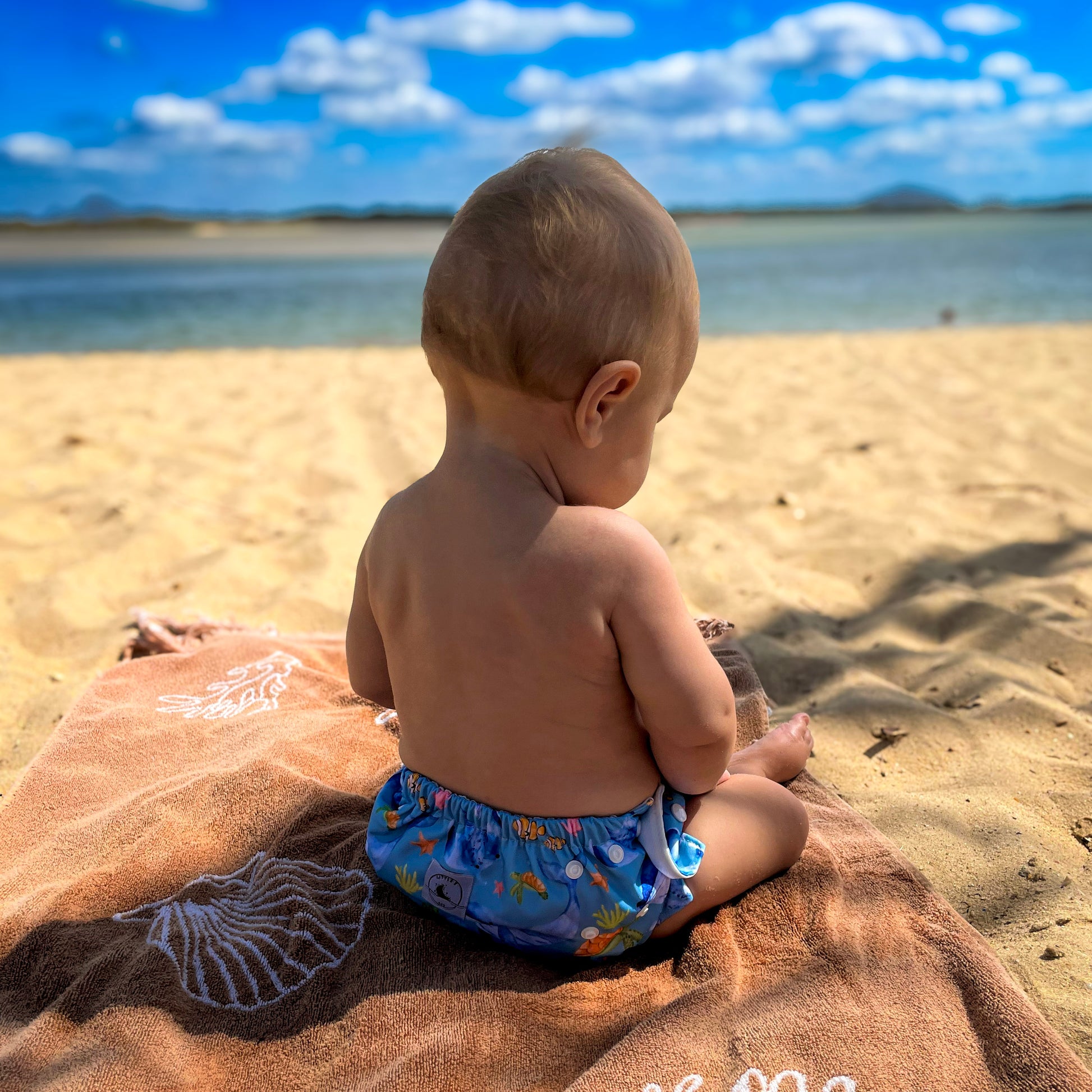 Swim nappy with ocean print worn by baby, featuring adjustable snaps and soft, water-friendly fabric.