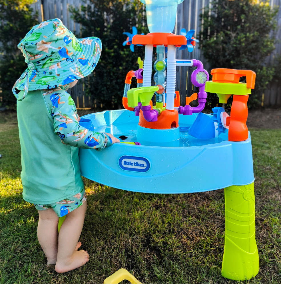 LITTLE E & CO – kids long-sleeve rash guard, a pastel purple with a green with a colourful rainforest print featuring birds, frogs, lizards and butterflies. Made with UPF 50+ sun protection fabric. The rash guard has a front zipper for easy wear.