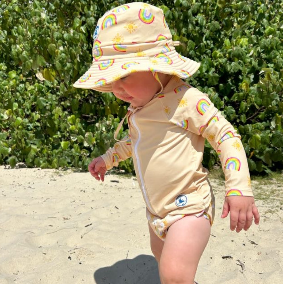 LITTLE E & CO – Children's rashie guard, a pale yellow with a colourful rainbow and sun print. Made with UPF 50+ sun protection fabric. The rash guard has a front zipper for easy wear.