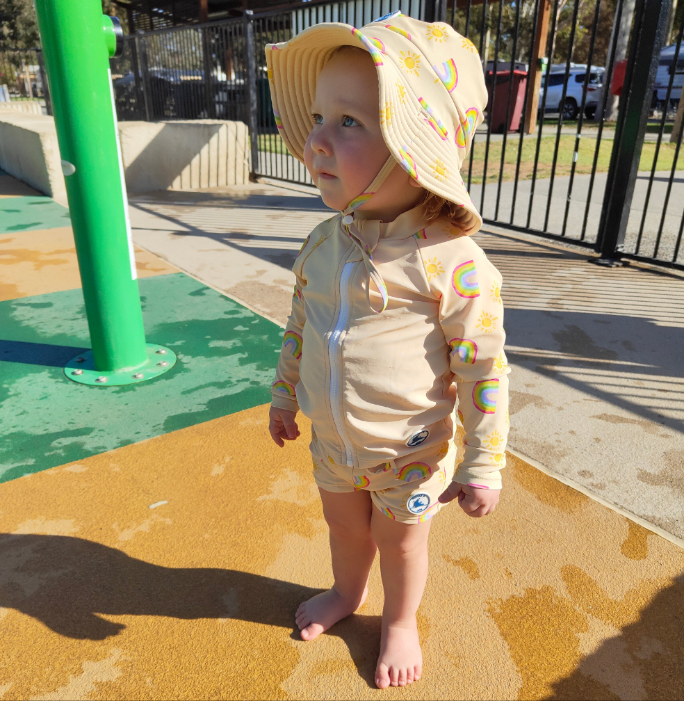 LITTLE E & CO – kids swim shorts, a pale yellow with a colourful rainbow and sun print. Made with UPF 50+ sun protection fabric. The shorts feature an adjustable drawstring waistband for a secure fit
