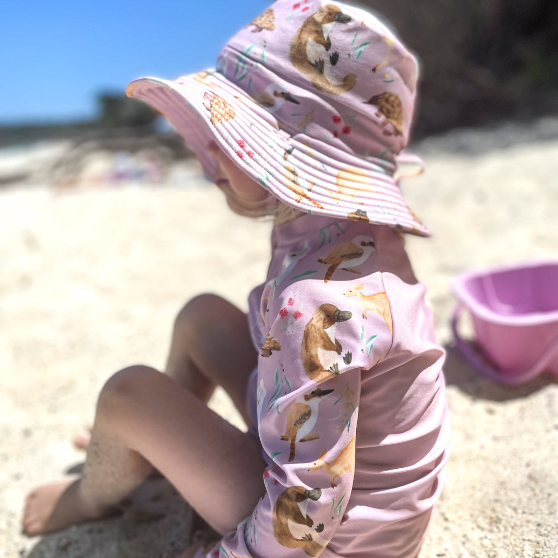 LITTLE E & CO – kids long-sleeve rash guard, a pale pink with a colourful Australian animals print featuring koalas, kangaroos, platypus, kookaburras and echidnas. Made with UPF 50+ sun protection fabric. The rash guard has a front zipper for easy wear.