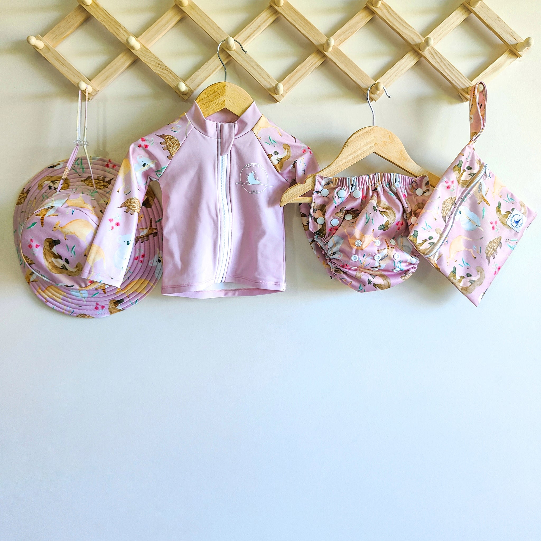 Baby swimwear set in pale pink with Australian animals print featuring rash guard, swim hat, reusable swim nappy and wet bag.