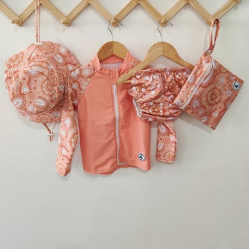 Baby Swimwear Set in peach pink with contemporary indigenous print, includes UPF 50+ long sleeve rashie with front zipper, adjustable swim nappy, sun hat with toggles, and matching wet bag.

