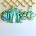 LITTLE E & CO - four-piece kids' swim set featuring a long-sleeve rash guard, swim hat, swim nappy and wet bag. The set is a green with a colourful rainforest print featuring birds, frogs, lizards and butterflies. Made with UPF 50+ sun protection fabric. The rash guard has a front zipper for easy wear, and the swim nappy has adjustable snaps, and the hat has adjustable toggles.