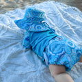LITTLE E & CO - four-piece kids' swim set featuring a long-sleeve rash guard, swim hat, swim nappy and wet bag. The set a turquoise blue with a colourful contemporary indigenous print. Made with UPF 50+ sun protection fabric. The rash guard has a front zipper for easy wear, and the swim nappy has adjustable snaps, and the hat has adjustable toggles.