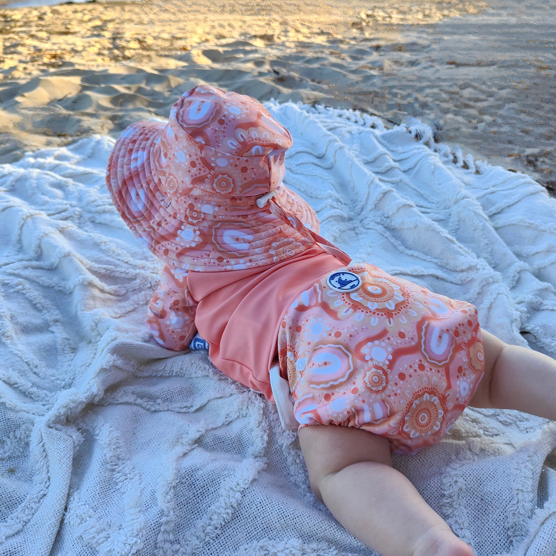 LITTLE E & CO – kids swim nappy, a peach pink with a colourful contemporary indigenous print. The swim nappy is a one size fits most design and has 3 adjustable snap settings.
