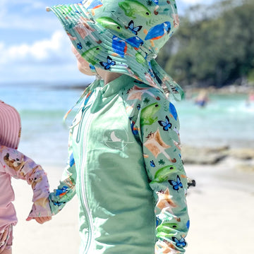 LITTLE E & CO - Two-piece kids' swim set featuring a long-sleeve rash guard and swim hat. The set a green with a colourful rainforest print featuring birds, frogs, lizards and butterflies. Made with UPF 50+ sun protection fabric. The rash guard has a front zipper for easy wear, and the hat features adjustable toggles.