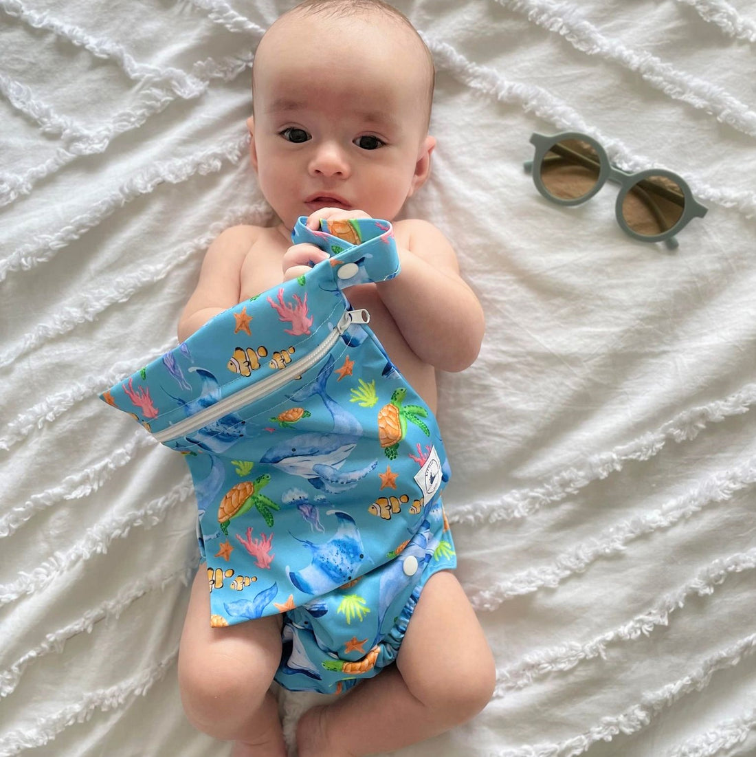 Swim Nappy and Wet Bag in blue ocean print with whales, turtles, fish, and coral, featuring one-size swim nappy with adjustable snaps and waterproof wet bag with strap.

