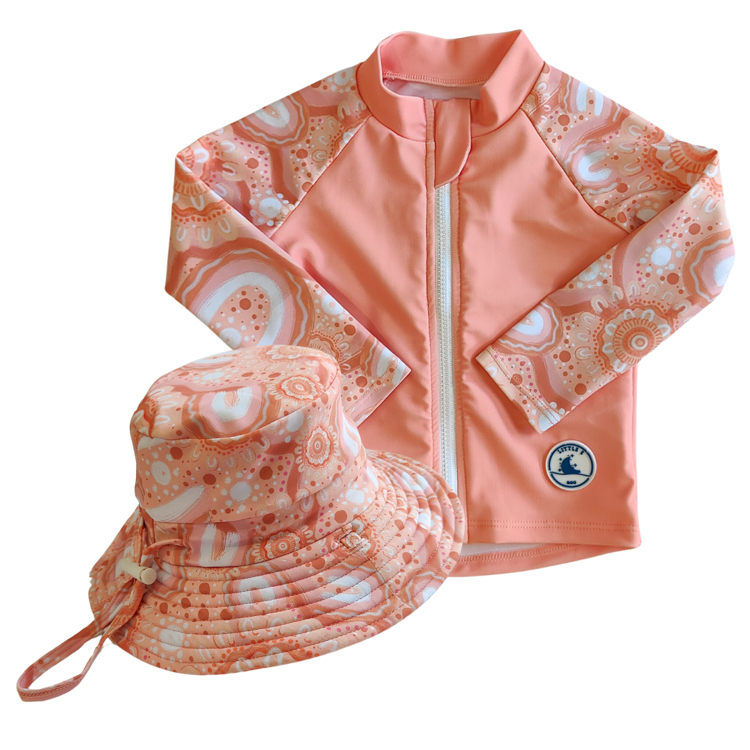 LITTLE E & CO - Two-piece kids' swim set featuring a long-sleeve rash guard and swim hat. The set is a peach pink with a colourful contemporary indigenous print. Made with UPF 50+ sun protection fabric. The rash guard has a front zipper for easy wear, and the hat features adjustable toggles.