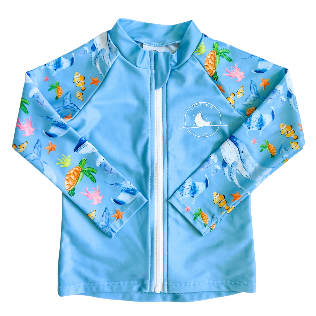 LITTLE E & CO – kids long-sleeve rash guard, a pastel purple with a blue with a colourful ocean print featuring whales, turtles, fish and coral. Made with UPF 50+ sun protection fabric. The rash guard has a front zipper for easy wear.