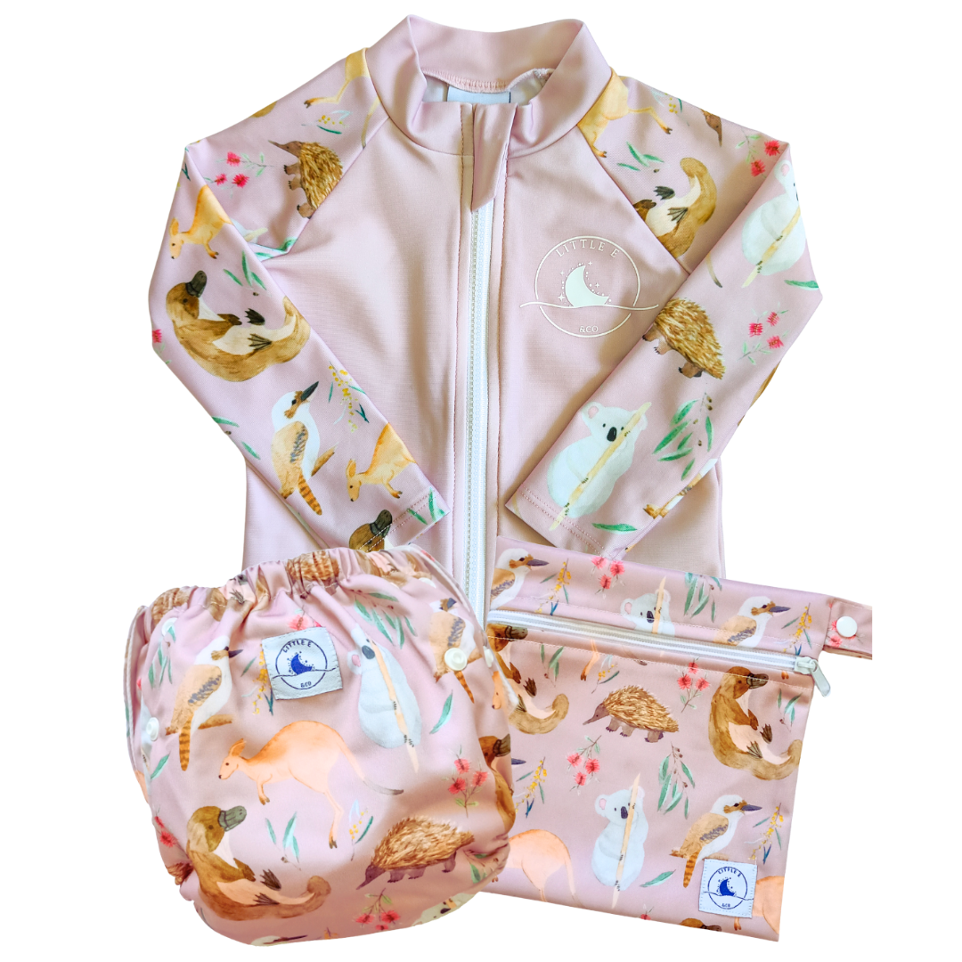LITTLE E & CO – Three-piece kids' swim set featuring a long-sleeve rash guard, swim nappy and wet bag. The set is a pale pink with a colourful Australian animals print featuring koalas, kangaroos, platypus, kookaburras and echidnas. Made with UPF 50+ sun protection fabric. The rash guard has a front zipper for easy wear, the swim nappy has adjustable snaps and the wet bag has a strap.