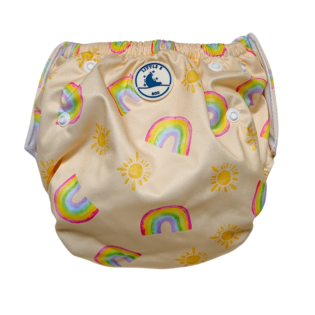 LITTLE E & CO – Three-piece kids' swim set featuring a long-sleeve rash guard, swim nappy and wet bag. The set is a pale yellow with a colourful rainbow and sun print. Made with UPF 50+ sun protection fabric. The rash guard has a front zipper for easy wear, the swim nappy has adjustable snaps and the wet bag has a strap.