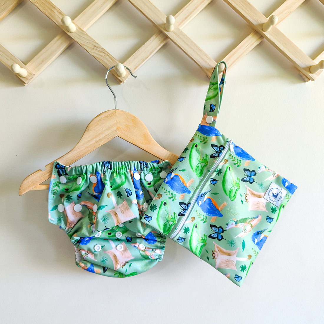 LITTLE E & CO – Three-piece kids' swim set featuring a long-sleeve rash guard, swim nappy and wet bag. The set is a green with a colourful rainforest print featuring birds, frogs, lizards and butterflies. Made with UPF 50+ sun protection fabric. The rash guard has a front zipper for easy wear, the swim nappy has adjustable snaps and the wet bag has a strap.