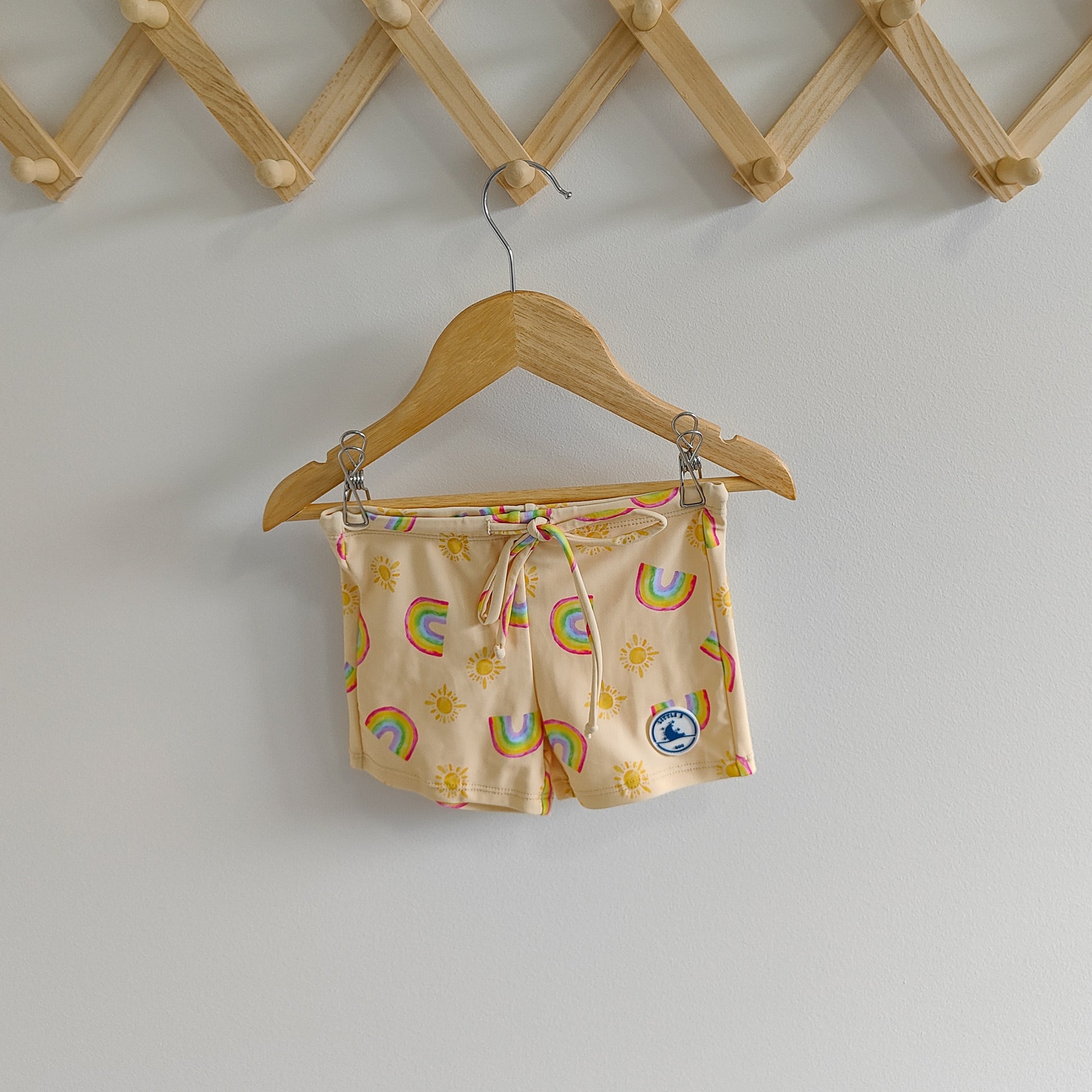 LITTLE E & CO – kids swim shorts, a pale yellow with a colourful rainbow and sun print. Made with UPF 50+ sun protection fabric. The shorts feature an adjustable drawstring waistband for a secure fit