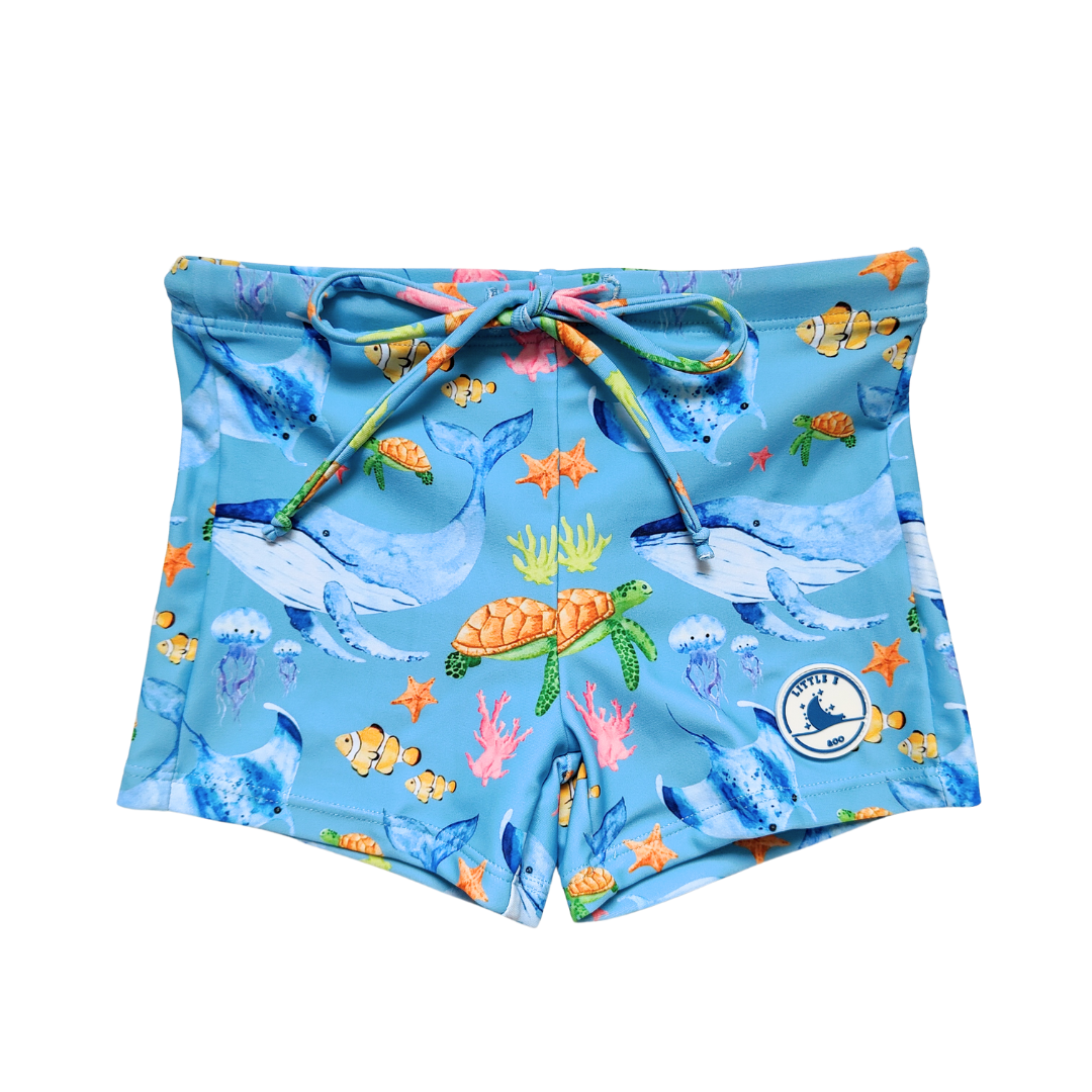 LITTLE E & CO – kids swim shorts, The set is blue with a colourful ocean print featuring whales, turtles, fish and coral. Made with UPF 50+ sun protection fabric. The shorts feature an adjustable drawstring waistband for a secure fit
