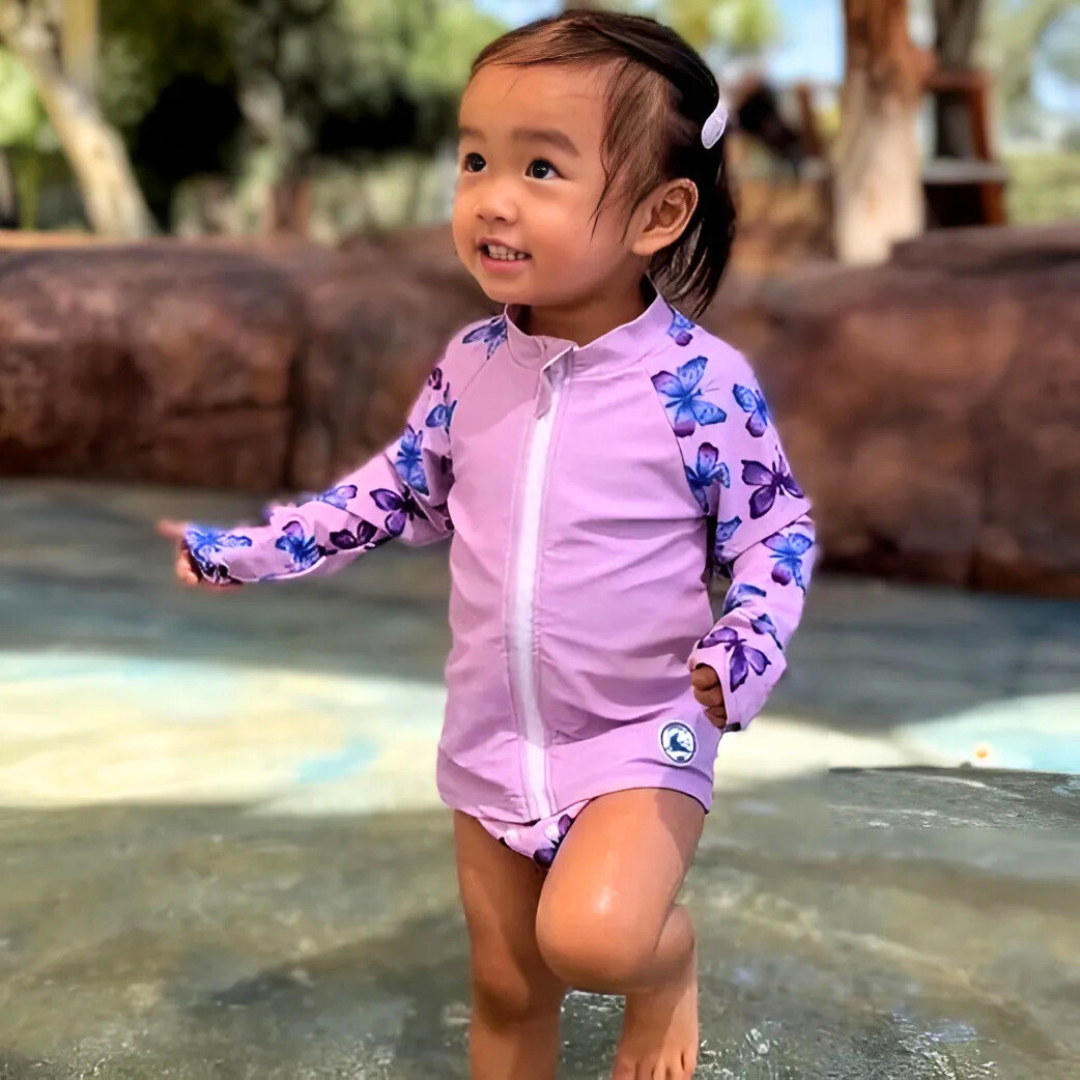 Baby swimwear set in butterflies print worn by toddler, featuring a long sleeve rashie and reusable swim nappy for sun-safe water play.